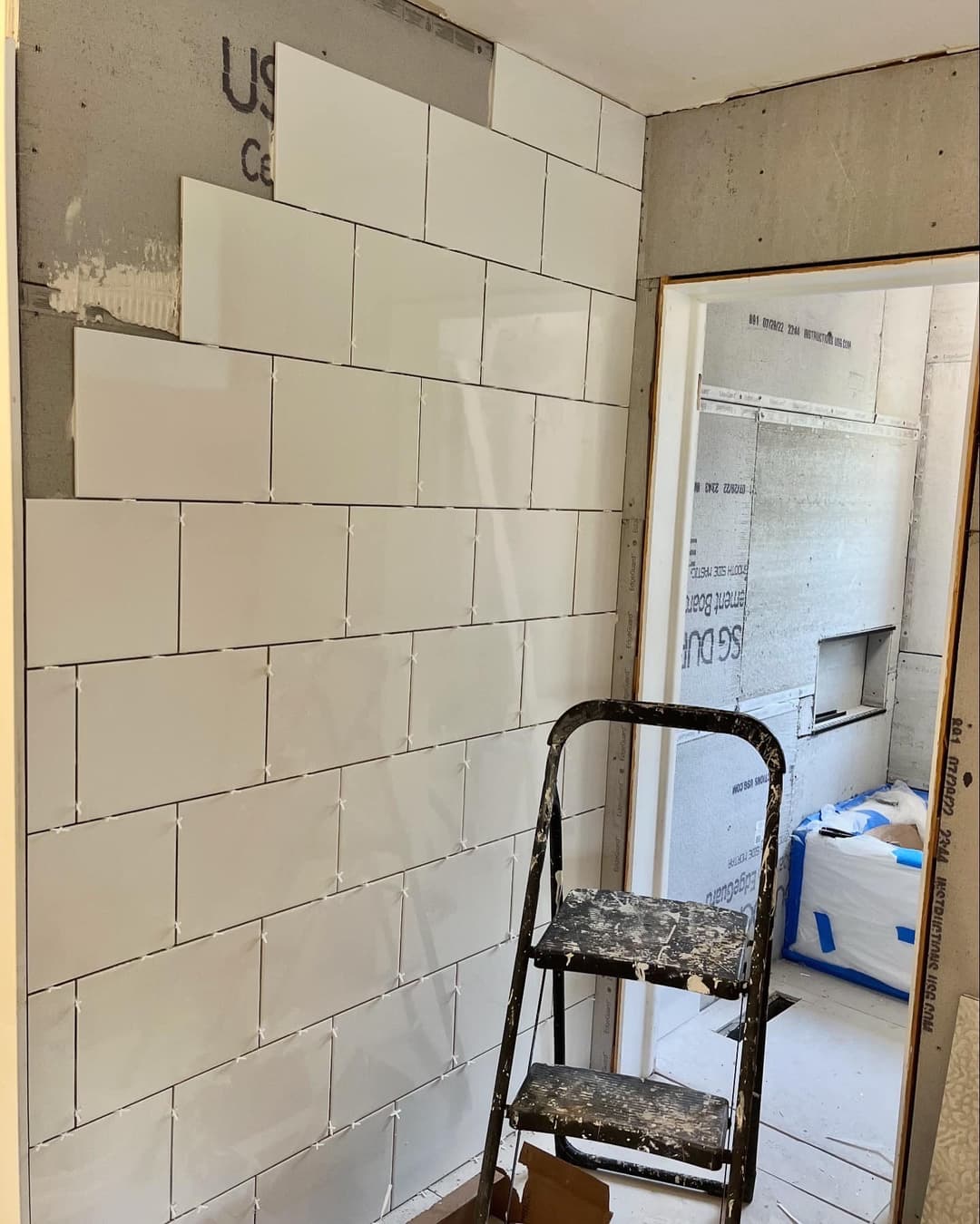 White tiles being installed on a wall, with a sturdy ladder in a renovation setting.