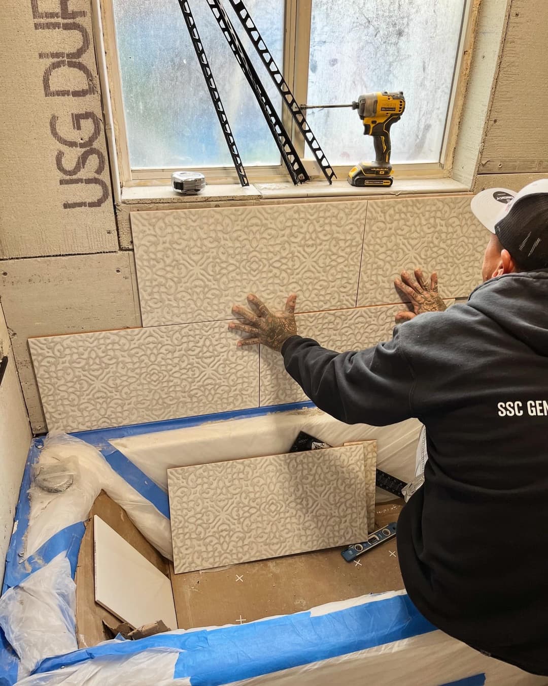 Tile installation process in a bathroom with patterned tiles and construction tools.