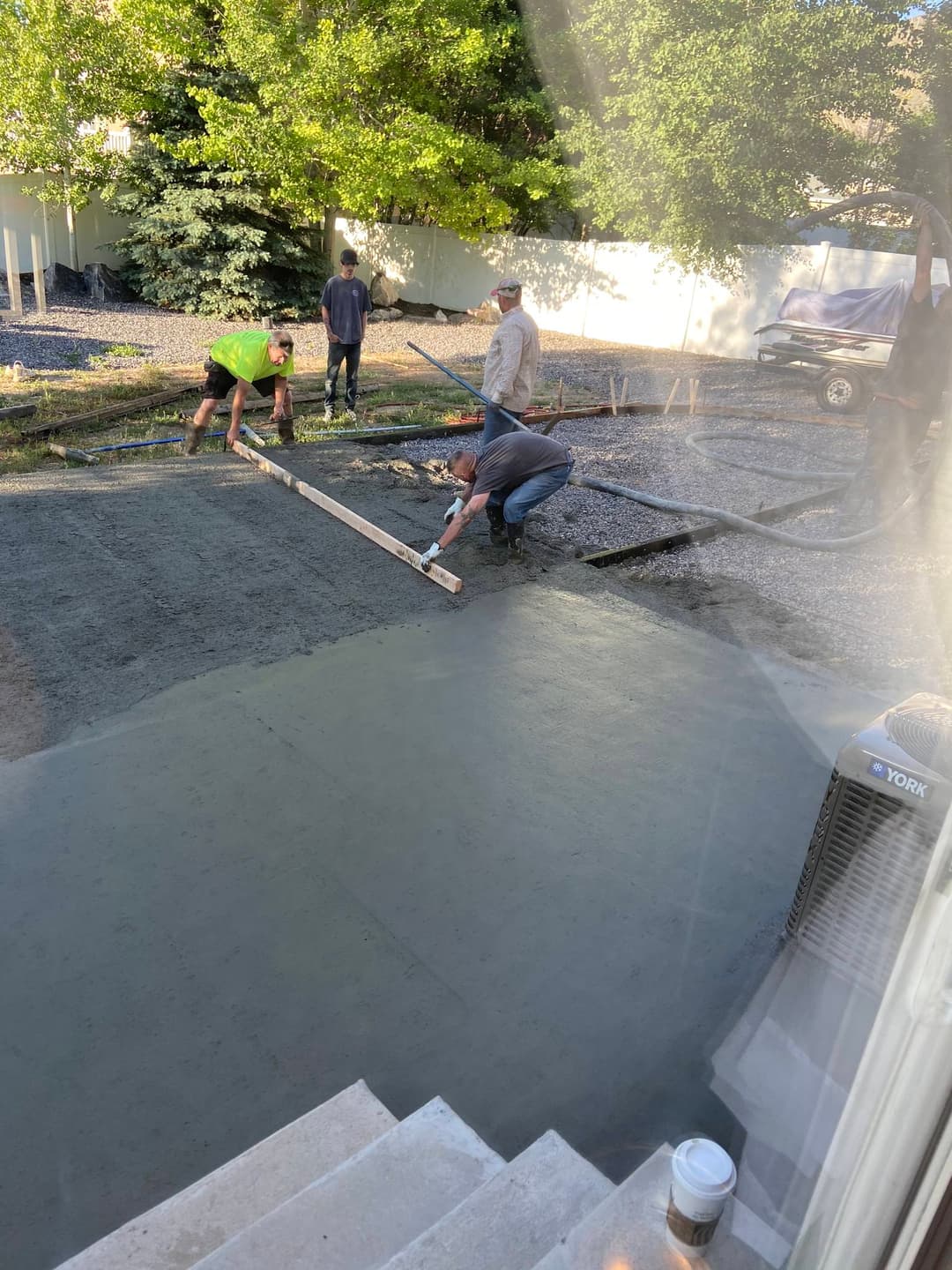 Workers pouring and smoothing concrete for a new patio in a residential yard.