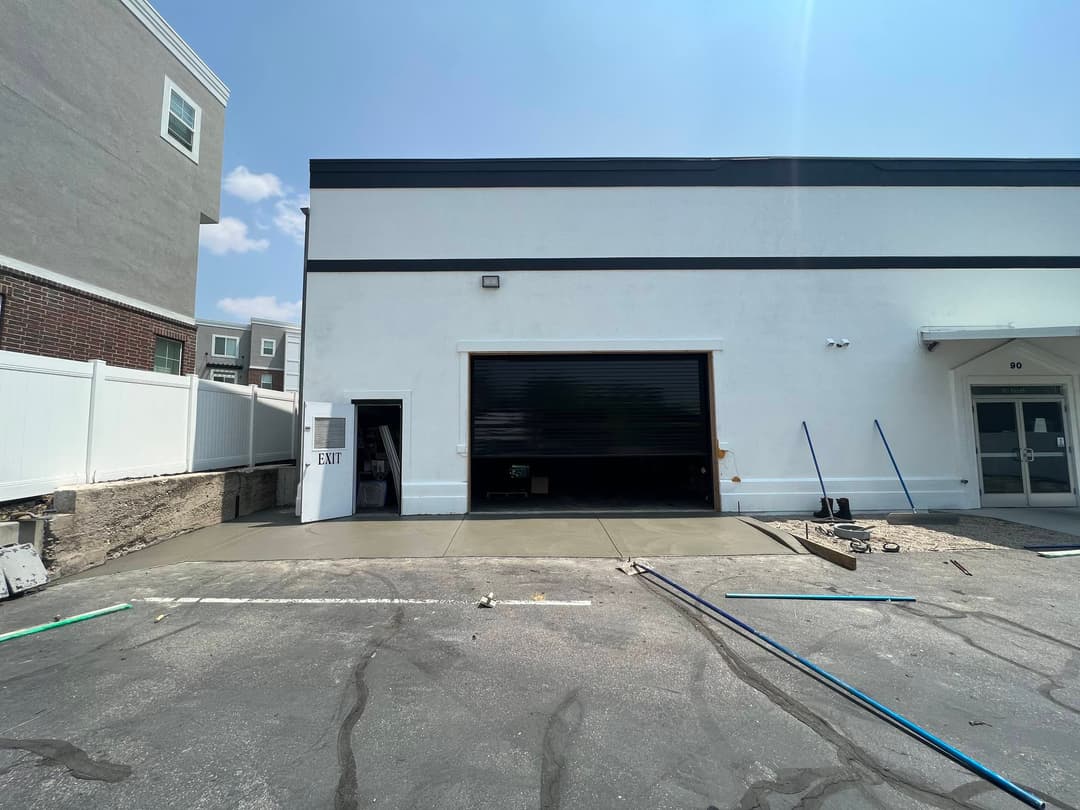 Exterior view of a warehouse with a large black roll-up door and clear sky above.