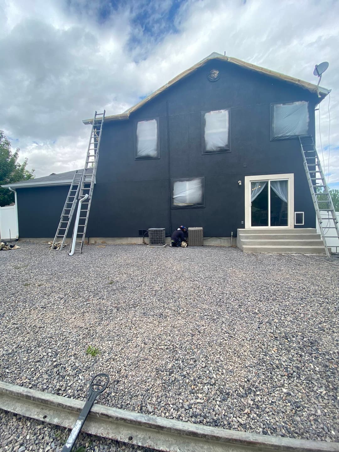 Black exterior house with workers on ladders and freshly painted windows, gravel foreground.