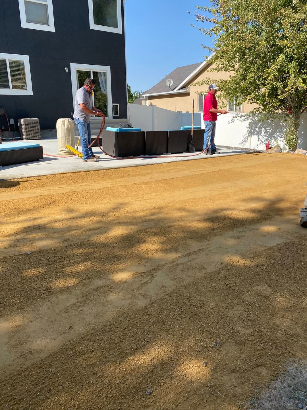 Workers preparing a backyard for landscaping with gravel and leveled soil.