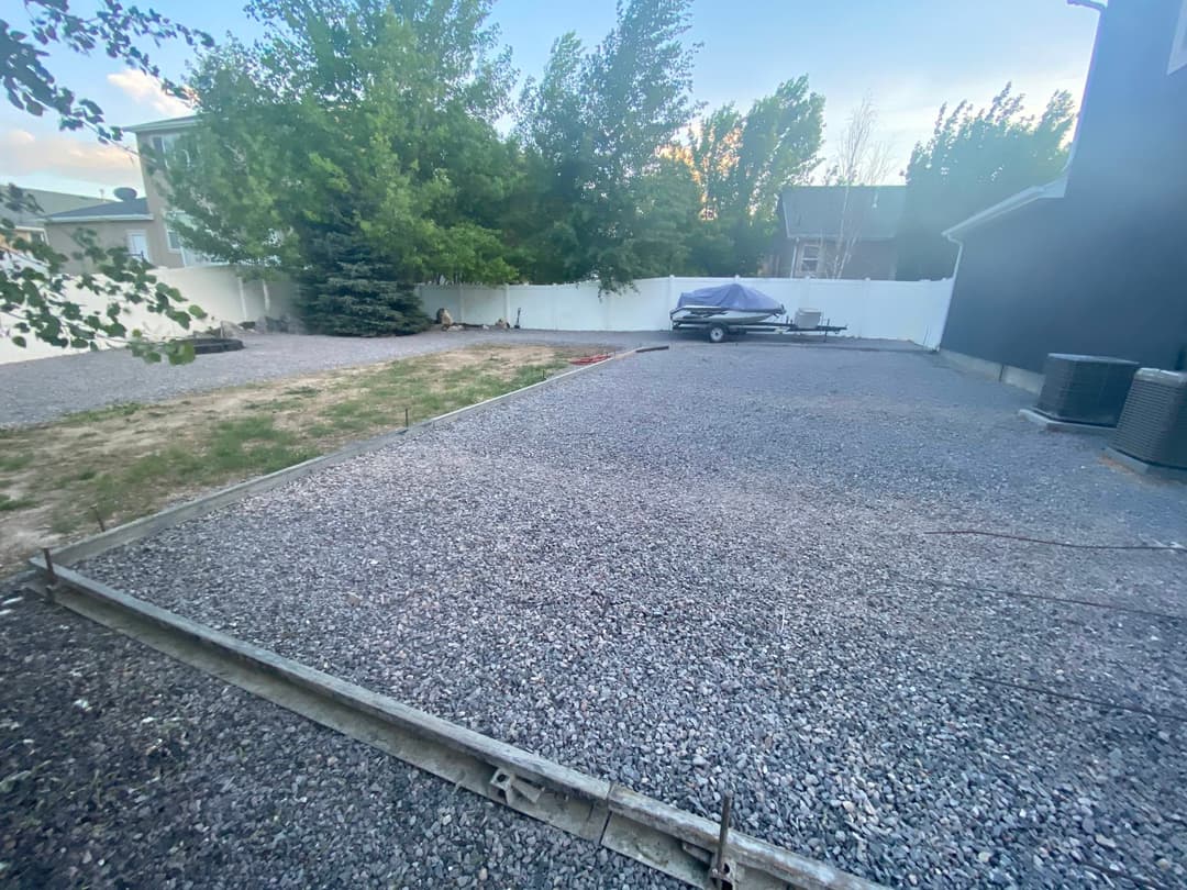 Gravel backyard space with boat, trees, and white fence in residential area.