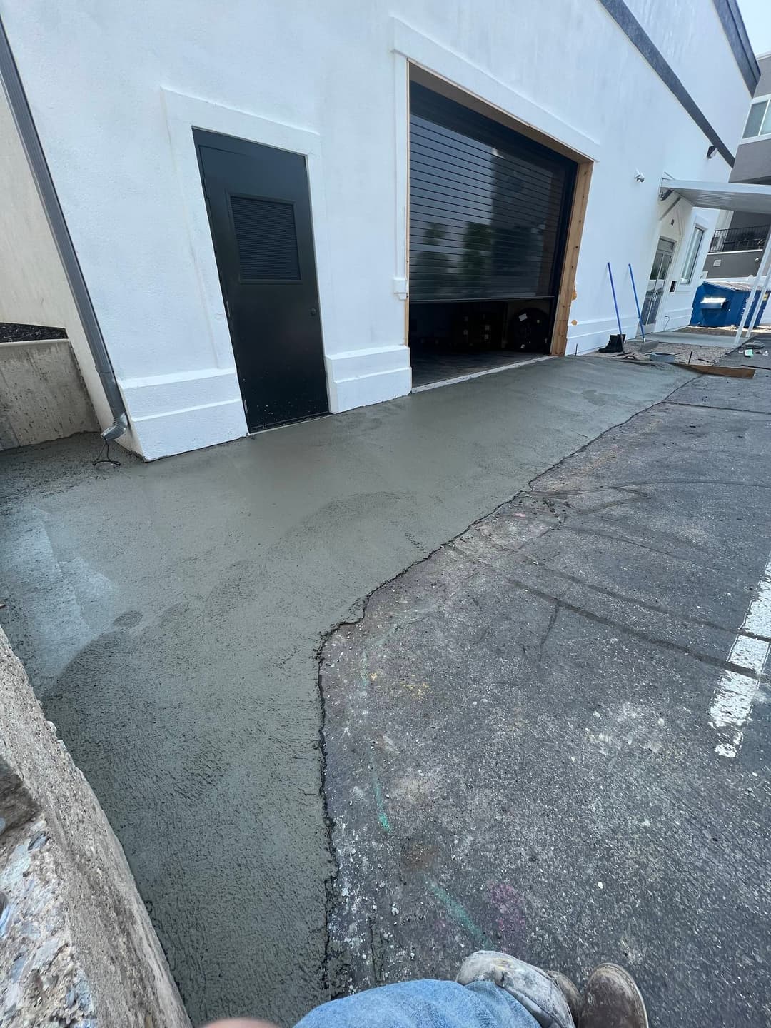 Freshly poured concrete sidewalk next to a commercial building entrance and loading dock.